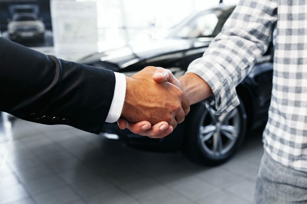 Customer shaking hands with professional car dealer at automobile dealership