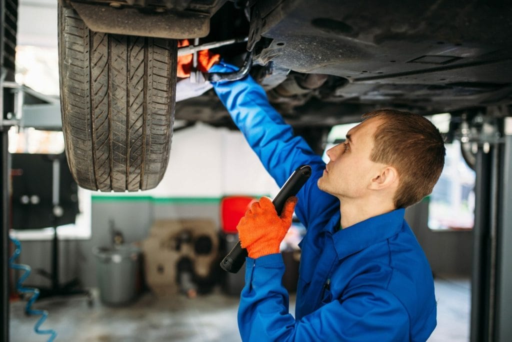 Mechanic with lamp checks the car suspension